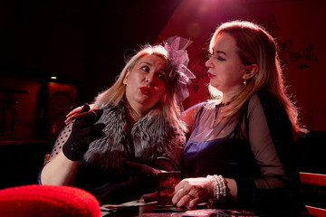 Two fat women with playing cards in a dark room with red light. Gangsters style