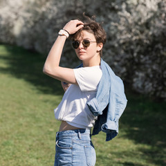 A young girl with a stylish short haircut against the backdrop of a blooming city park.