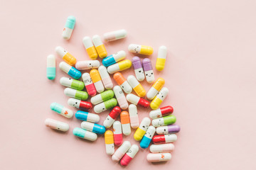 Pile of funny colored capsule on a pastel paper pink background.