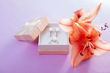 Set of pearl jewellery in the gift box with flowers. Earrings and ring with lily on purple background