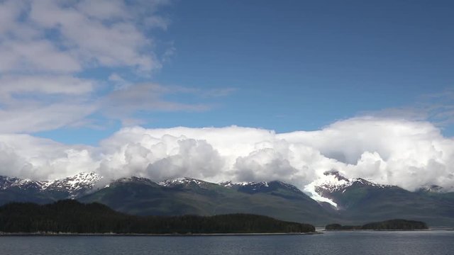 Receding glacier on side of mountains. Cumulus Clouds Over Mountainous Landscape on Waterfront.