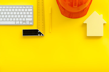 Constructor office desk with tools, helmet, ruler, keyboard and house figure on yellow background top view mock-up