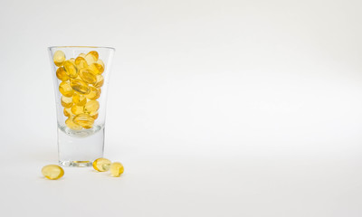 Front view on small glass of oil capsules with omega 3, vitamin D. Oil golden capsules scattered isolated on white background. Healthy life concept with copy space for text. Healthy supplement pills.