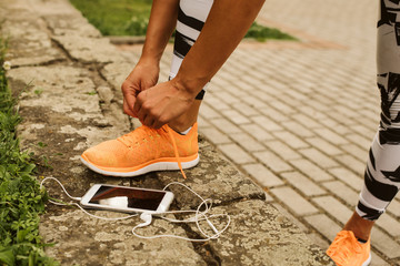 A fitness girl, orange sneakers and her phone. Training in the park