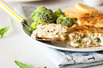 Delicious cutlets (fish or meat) with broccoli, potatoes and sauce on a plate. Light grey stone background. 