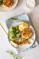 Delicious cutlets (fish or meat) with broccoli, potatoes and sauce on a plate. Light grey stone background. 