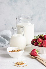 Healthy breakfast ingredients. Homemade granola, milk or yogurt in jugs, strawberries and rosemary on light stone background.