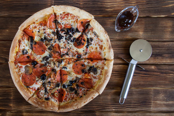 Homemade pizza with salami, mushrooms and olives lies on a plank table next to a special circular knife and picnic sauce. Autumn Farm Fair