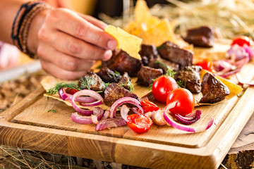 slices of fried meat with onions and cherry tomatoes on a thin flat cake. Female hand takes a piece of cake. Horizontal, bright colors, space for text
