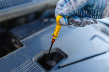 Close-up car mechanic's hands in gray gloves holding dipstick of oil level in the engine. Auto mechanic checks oil level in car engine.