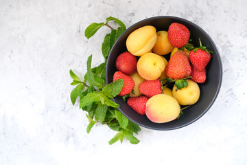Sweet strawberries and apricot decorated mint leaves, top view.  Fresh summer fruits in bowl.