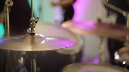 The drummer plays the drums, strikes the musical plates at the concert with his chopsticks. Concert performance on stage. Color light illuminates the cymbals of the drum set in close-up.