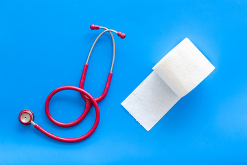 Toilet paper roll and stethoscope for proctology diseases concept on blue background top view