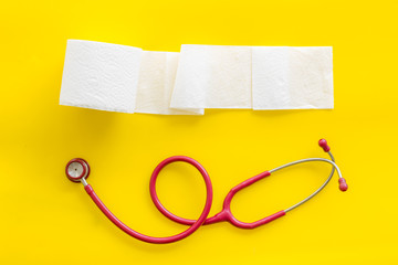 Toilet paper roll and stethoscope for proctology diseases concept on yellow background top view