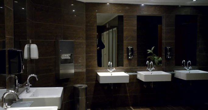 bald man dressed in business suit approaching to washbasin in public toilet, cheering himself in mirror