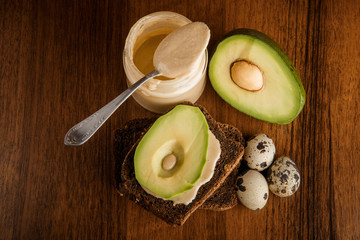 top view of quail eggs, sliced avocado on rye bread, tahini jar