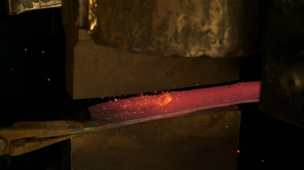 CLOSE UP: Orange sparks fly off the hot piece of metal being forged into blade.