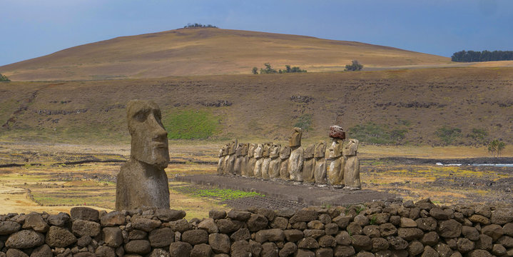 Mysterious monolithic structures with a human face are behind low wall of rocks.