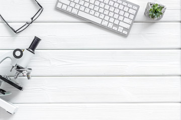 Medical tests on work desk of doctor with microscope, keyboard, glasses on white wooden background top view copyspace