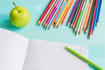 Naklejka premium Concept back to school.School accessories, colored pencils, pen with empty notebook on blue wooden background.