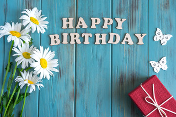 Happy birthday inscription. Natural daisies on a wooden background with the inscription Happy Birthday. Greeting card design. Floral background. Flat lay, top view.