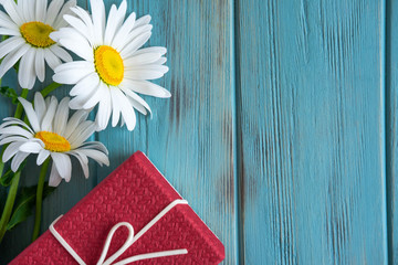 Obraz premium Background for greeting card with daisies on a wooden background and a gift. Frame for text with daisies on a wooden background. Floral background banner. Flat lay, top view.