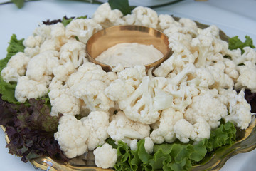 Fresh cauliflower with cheese sauce and salad leaves on table, close-up.