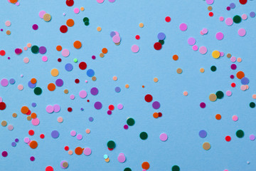 Multicolored round sequins on a pastel blue background with confetti.