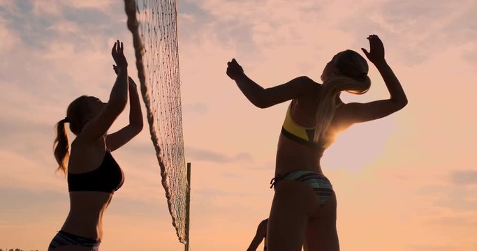 Group of young girls playing beach volleyball during sunset or sunrise, slow motion,