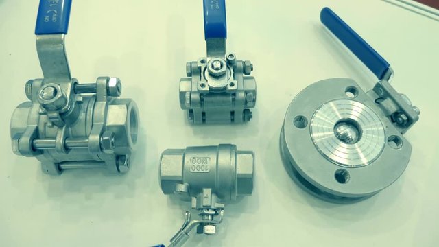 Shiny ball valves lie on a white surface. A new samples is presented for review at the exhibition. Shot in motion