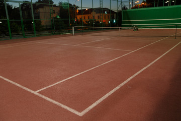 An empty tennis court at night, lit by bright lights