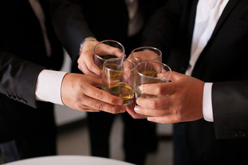 Close-up portrailt view of two men in formal wear, clinking whiskey glasses
