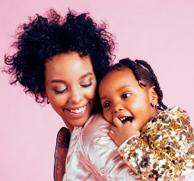 young pretty african-american mother with little cute daughter hugging, happy smiling on pink background, lifestyle modern people concept close up