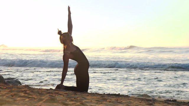 beautiful girl changes yoga pose back bending on yellow sand beach against endless ocean with huge foaming waves slow motion. Concept fitness sport yoga healthy lifestyle