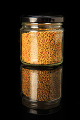 bee pollen grain in small glass jar over black background