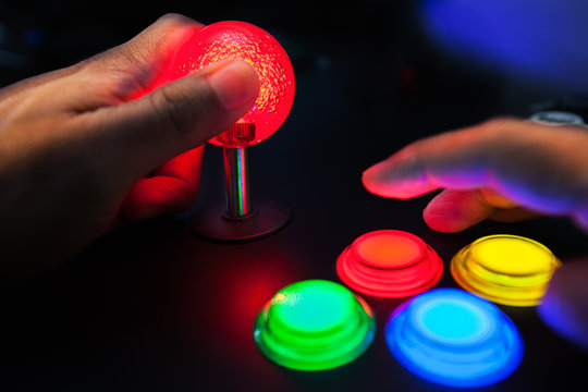 A red lighted arcade joystick and four button layout push buttons being played by a video gamer on a retro arcade machine.