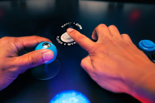 The hands of an arcade player reaching for the player one start button and holding a top fire four way joystick.