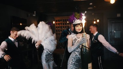 Retro theme party - Young people having fun - A woman holding a huge bottle of champagne with fireworks on top