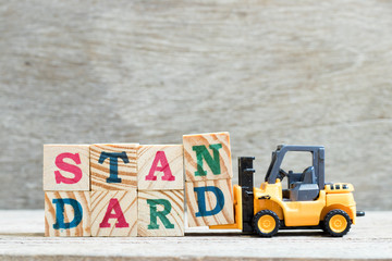 Toy forklift hold letter block n, d to complete word standard on wood background