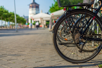 Fototapeta na wymiar Close up low angle view of bicycle's wheel at public bike parking on the street at Rheinufer Promenade, waterside of Rhine river, with blur background of maritime museum in Düsseldorf, Germany. 