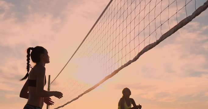 Young female volleyball players pass and spike the ball over the net on a sunny summer evening. Fit Caucasian girls playing beach volleyball at sunset