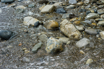 pebble stones on the sea beach, the rolling waves of the sea with foam