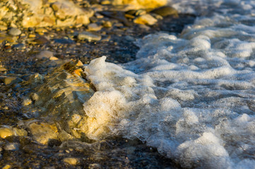 pebble stones on the sea beach, the rolling waves of the sea with foam