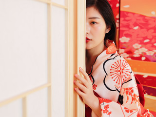 Portrait of attractive Chinese woman wearing traditional Japanese Kimono, looking at camera behind traditional wood and paper door, oriental beauty.