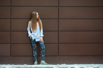 Portrait of a young pretty caucasian teenage girl with long hair in a blue shirt opposite brown background.