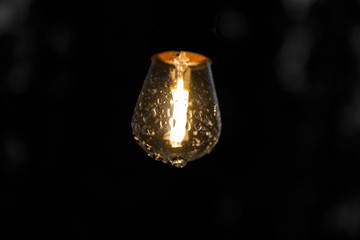 Close up on outdoor  lit lightbulb with droplets of rain on the glass