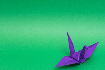 purple origami paper crane on green background