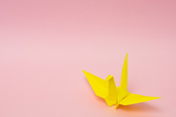 yellow origami paper crane on pink background