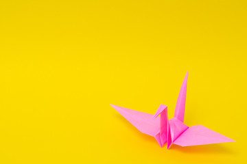 pink origami paper crane on yellow background