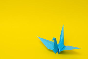 light blue origami paper crane on yellow background